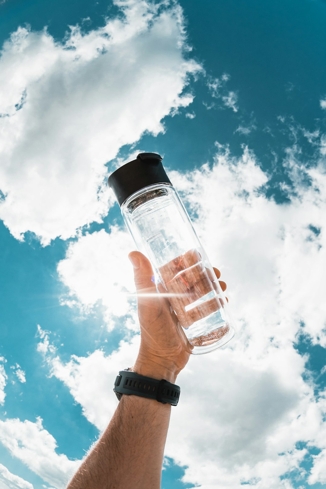 a-hand-holding-a-water-bottle-in-front-of-a-blue-sky-rvezdpcela0